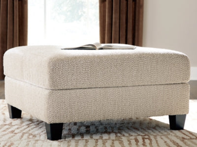 Steelwater Retreat oversized accent ottoman by Ashley Furniture with plush fabric and wooden block legs, shown in a cozy living room setting.